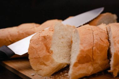 Bıçaklı dilimlenmiş beyaz ekmek tahta bir arka planda kesim tahtasının üzerinde yatıyor.
