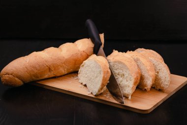 Bıçaklı dilimlenmiş beyaz ekmek tahta bir arka planda kesim tahtasının üzerinde yatıyor.