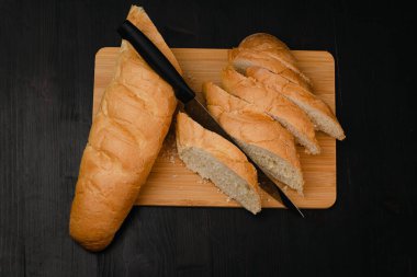 Bıçaklı dilimlenmiş beyaz ekmek tahta bir arka planda kesim tahtasının üzerinde yatıyor.