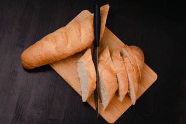 Bıçaklı dilimlenmiş beyaz ekmek tahta bir arka planda kesim tahtasının üzerinde yatıyor.