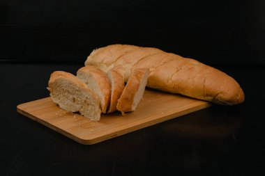Dilimlenmiş beyaz ekmek tahta bir arka planda kesim tahtasının üzerinde yatıyor.