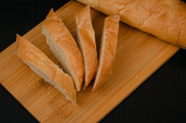 Dilimlenmiş beyaz ekmek tahta bir arka planda kesim tahtasının üzerinde yatıyor.