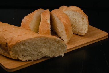 Dilimlenmiş beyaz ekmek tahta bir arka planda kesim tahtasının üzerinde yatıyor.