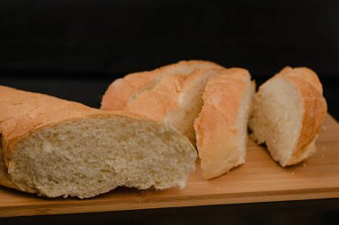 Dilimlenmiş beyaz ekmek tahta bir arka planda kesim tahtasının üzerinde yatıyor.