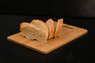 Dilimlenmiş beyaz ekmek tahta bir arka planda kesim tahtasının üzerinde yatıyor.