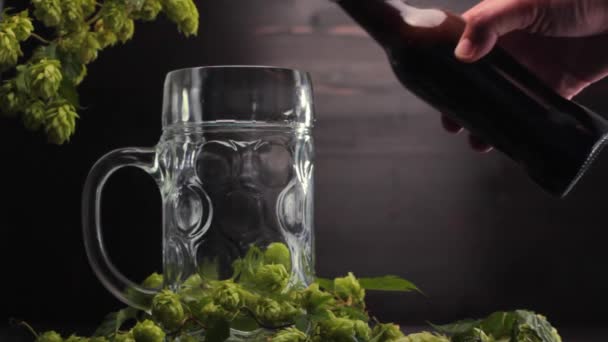 男人的手把啤酒从瓶子里倒进木制背景的大啤酒杯里 — 图库视频影像