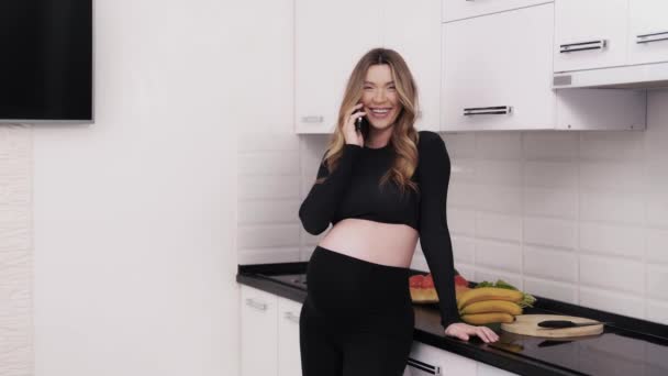 漂亮的孕妇在家里有一个友好的电话交谈 在厨房里谈话时 她笑得很开心 — 图库视频影像