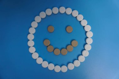 Mavi arka plandaki haplardan yapılmış olumlu bir gülümseme. İlaç, ilaç, tedavi, sağlık sigortası. Mutlu konsept