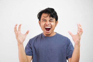 Beyaz arka planda dikilen rahat tişört giyen yakışıklı Asyalı genç adam agresif bir ifadeyle çılgınca bağırıyor ve ellerini kaldırıyordu. Hayal kırıklığı konsepti.