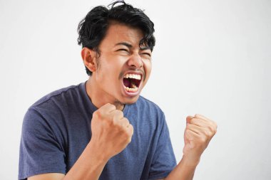 Kızgın, agresif, Asyalı, tişört giyen, lacivert renkte vahşi bir ifadeyle bağıran ve kızgın yumruklar sallayan genç bir adam.