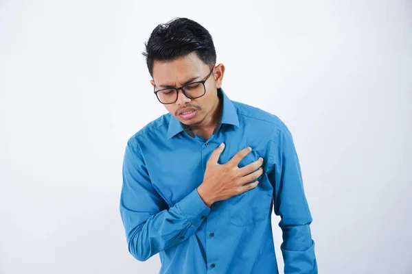 Asian young man with glasses holding his chest in chest pain or coronary heart disease wearing blue shirt isolated on white background