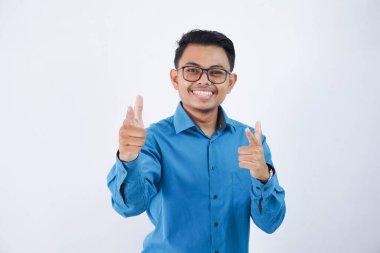 Yakışıklı Asyalı, gözlüklü, parmağıyla öne doğru gülümseyen, beyaz arka planda izole edilmiş mavi gömlekli bir adam.