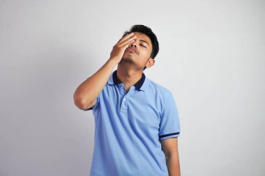 Baş dönmesi ya da stres portresi. Beyaz arka planda izole edilmiş mavi polo tişört giyen Asyalı genç adam.