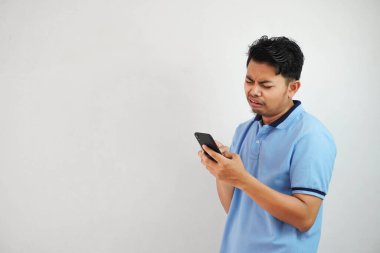 Beyaz arka planda mavi polo tişört giyen Asyalı genç bir adamı tutan üzgün surat. Rahatsız edici yüz ifadeleri