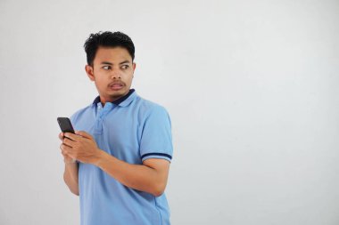 Beyaz arka planda izole edilmiş mavi polo tişört giyen Asyalı genç bir adamı tutmaya çalışmaktan hoşlanmamanın ifadesi.