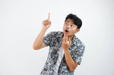 shocked Asian man holding chin gesture point finger up and looking up wearing black shirt isolated on white background