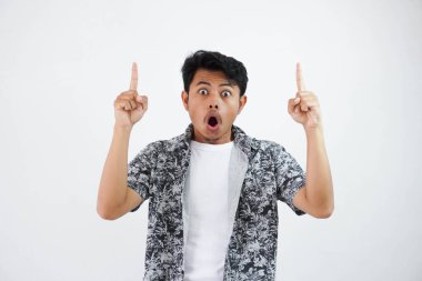 shock young Asian man pointing up with big eyes and mouth open, shocked surprised expression isolated