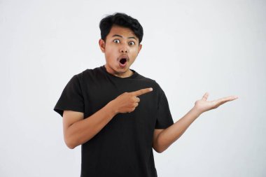 shocked asian man with fingers pointing to the side wearing black t shirt isolated on white background