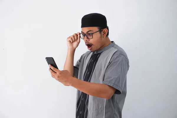 Wstrząśnięty Azjatycki Muzułmanin Trzyma Telefon Okulary Nosząc Szare Muzułmańskie Ubrania — Zdjęcie stockowe