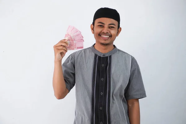 笑顔や幸せな若いアジアのイスラム教徒の男保持紙幣ギフト Thr から家族Ramadan Fitr時間身に着けていますグレーイスラム教徒の服白い背景に隔離 — ストック写真