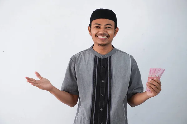 笑顔や幸せな若いアジアのイスラム教徒の男性を保持し 紙幣ギフトを指す Thr 家族ラマダーンイード フィトル時間から白い背景に隔離された灰色のイスラム教徒の服を着て — ストック写真