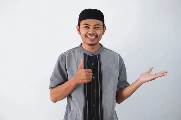 笑顔や幸せそうなアジア系ムスリム男性が手の平を見せ白い背景に隔離されたココの服を着て親指を立ててOkジェスチャーをする — ストック写真