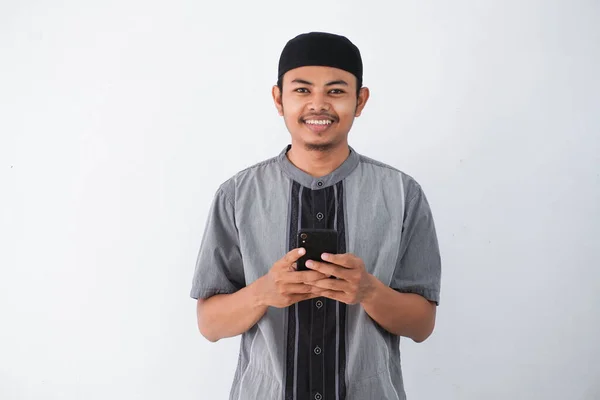 白い背景に隔離されたココの服を着て 携帯電話のルッキングカメラを持っている幸せや笑顔の若いアジアのイスラム教徒の男性 ラマダーンの概念 — ストック写真