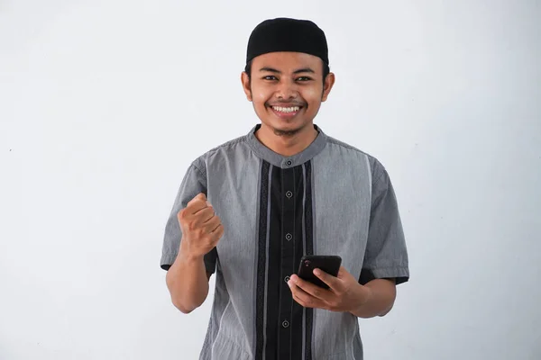 Uśmiechnięty Azjatycki Muzułmanin Człowiek Gospodarstwa Smartfon Wygląda Aparat Pięść Robi — Zdjęcie stockowe