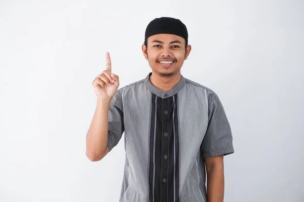 若いアジア系イスラム教徒の男性の指を上げて指を上げると 白い背景に隔離された灰色のココの服を着た笑顔に驚きました — ストック写真
