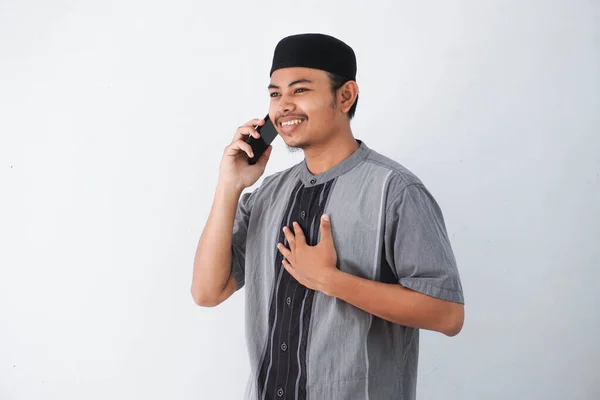 胸を背負った若いアジア系ムスリム男性の笑顔と白い背景に隔離されたココの服を着た携帯電話による電話通話 — ストック写真