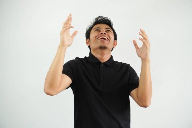 Siyah polo tişört giyen mutlu Asyalı bir genç beyaz arka planda zaferi ya da başarıyı kutluyor. Şaşırdı ve şok oldu..