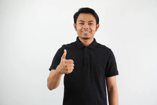 笑顔の若いアジア人男性の肖像画は 白い背景に隔離された黒いポロTシャツを着用して親指を与えます — ストック写真