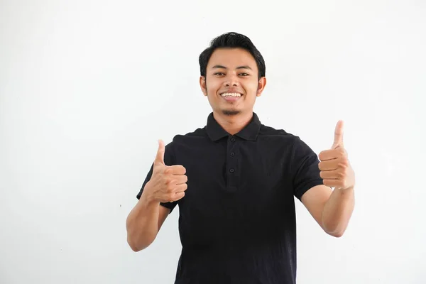 白い背景に隔離された黒いポロTシャツを身に着けている2つの親指を与える幸せか微笑む若いアジアの男 — ストック写真