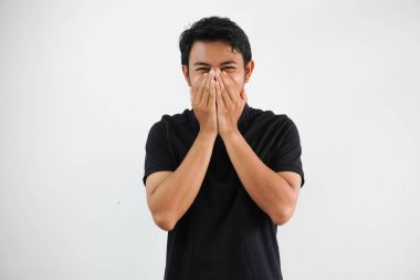 Gülümseyen Asyalı genç adam, beyaz arka planda izole edilmiş, utanmış, elleri siyah polo tişört giymiş, ağzı kapalı..