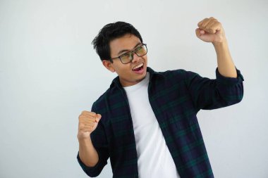 young asian man screaming success with his fist clenched isolated on white background clipart