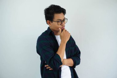 Asyalı genç adam kasvetli bir yüz ifadesi sergiliyor. Beyaz arka planda tek başına çenesini tutuyor.