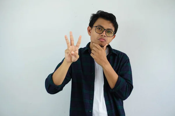 Νεαρός Ασιάτης Δείχνει Περίεργη Έκφραση Προσώπου Ενώ Δίνει Τρία Δάχτυλα — Φωτογραφία Αρχείου