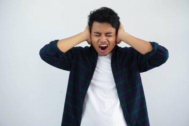 Asyalı genç adam öfkeli bir yüz ifadesi sergilerken iki eli de beyaz arka planda izole bir şekilde kulaklarını kapatıyor.