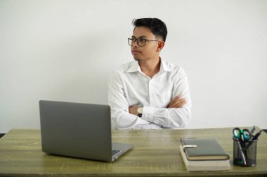 İş yerindeki genç Asyalı işadamı kollarını kavuşturup yan tarafa bakıyor ve gözlüklü beyaz gömlek giyiyor.