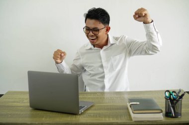 Genç Asyalı işadamı zaferi kutluyor. Gözlüklü beyaz gömlek giyiyor.