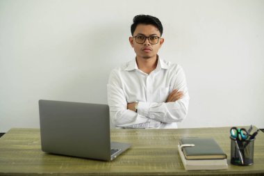 İş yerindeki genç Asyalı işadamı çapraz ellerle üzgün, gözlüklü beyaz gömlek giyiyor.