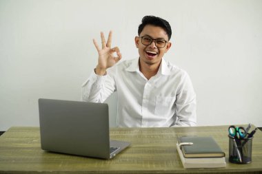 İş yerindeki genç Asyalı işadamı şaşırdı ve tamam işareti gösterdi, gözlüklü beyaz gömlek giyiyordu.