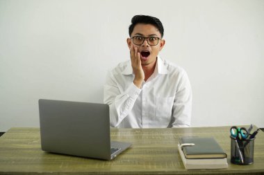 Genç Asyalı iş adamı, şaşırmış ve şok olmuş bir yüz ifadesiyle, gözlüklü beyaz gömlek giyiyor.