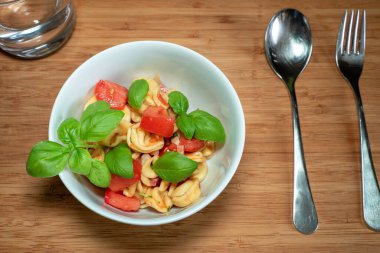 Tortellini salatası küçük bir kâse içinde çatal bıçak takımı ve ahşap bir masada bir bardak su.