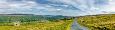 Yorkshire Dales tepelerinin manzarası. Yalnız taş binası ve bulutlu mavi gökyüzü.