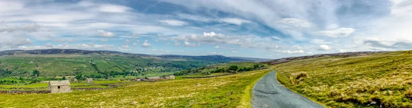 Yorkshire Dales tepelerinin manzarası. Yalnız taş binası ve bulutlu mavi gökyüzü.