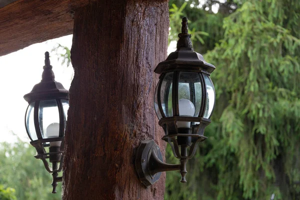 茶色の木製の柱には古い様式の金属製の提灯が取り付けられ 背景には緑の木がある — ストック写真