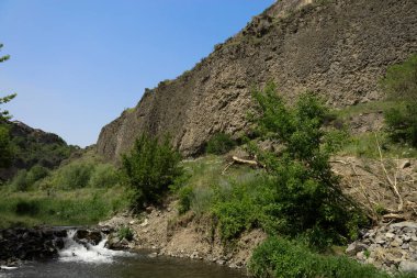 Yazın arka planında yüksek kayalar olan küçük bir şelale.