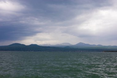 Bulutlu havada Sevan Gölü 'nde fırtına bulutları ve arka planda dağlar.