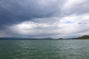 Bulutlu havada Sevan Gölü 'nde fırtına bulutları ve arka planda dağlar.